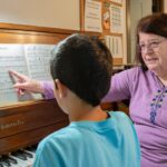 Kastanopolous guides a student through a piano lesson, drawing on decades of experience as a music teacher.